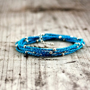 May include: A turquoise blue braided cord bracelet with silver beads.