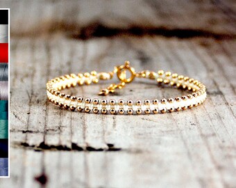 May include: A delicate gold and white beaded bracelet with a simple clasp. The bracelet is made with small, round beads and has a minimalist design.