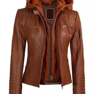 May include: A brown leather jacket with a detachable hood. The jacket features a zip-up front, multiple pockets, and decorative stitching on the shoulders and sleeves. The inner lining is a darker shade of brown.