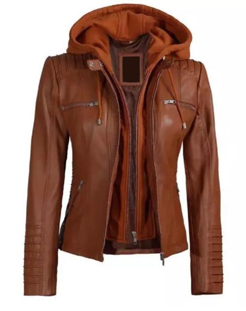 May include: A brown leather jacket with a detachable hood. The jacket features a zip-up front, multiple pockets, and decorative stitching on the shoulders and sleeves. The inner lining is a darker shade of brown.