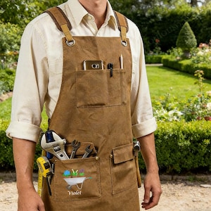 Puede incluir: Delantal de lona marrón con múltiples bolsillos, que contiene herramientas, un teléfono y un lápiz. El delantal tiene correas ajustables y herrajes metálicos. El bolsillo inferior presenta un gráfico de carretilla con el nombre "Violet".