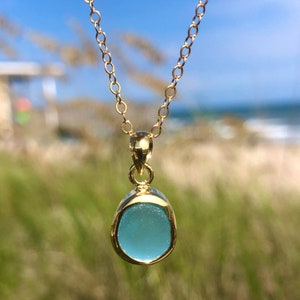 May include: A gold chain necklace with a light blue sea glass pendant