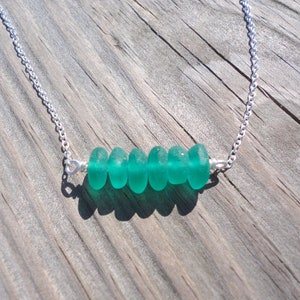 May include: A silver chain necklace with a row of five teal sea glass beads.