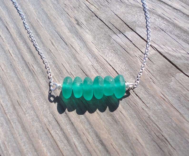 May include: A silver chain necklace with a row of five teal sea glass beads.