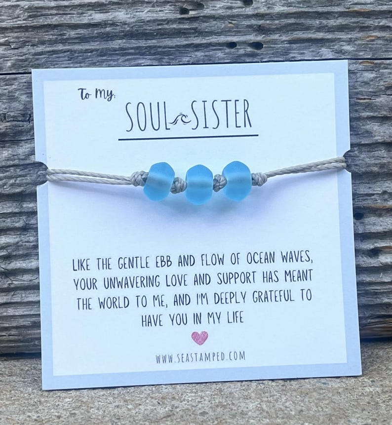 Może przedstawiać: Biała kartka z tekstem "To my Soul Sister" i wiadomością o przypływie i odpływie oceanicznych fal. Kartka ozdobiona jest jasnoniebieskim bransoletką z koralik&oacute;w.