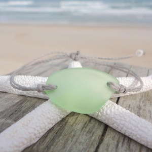 Peut inclure: Un bracelet en cordon gris avec un charme en verre de mer vert clair. Le bracelet est pr&eacute;sent&eacute; sur une &eacute;toile de mer blanche.