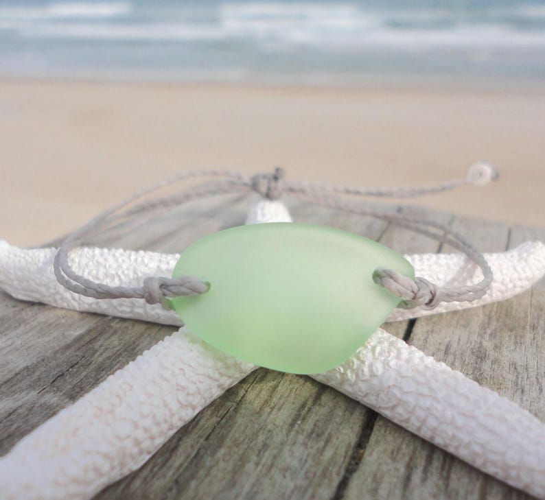 Peut inclure: Un bracelet en cordon gris avec un charme en verre de mer vert clair. Le bracelet est pr&eacute;sent&eacute; sur une &eacute;toile de mer blanche.