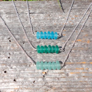 May include: Three silver necklaces with different shades of blue and green sea glass beads. Each necklace has six beads in a row.