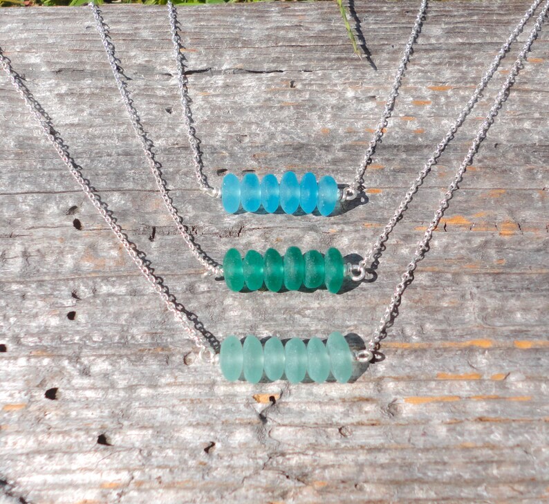 May include: Three silver necklaces with different shades of blue and green sea glass beads. Each necklace has six beads in a row.