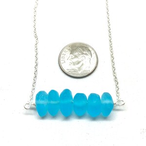 May include: A silver chain necklace with a row of light blue sea glass beads. The necklace is about the size of a dime.