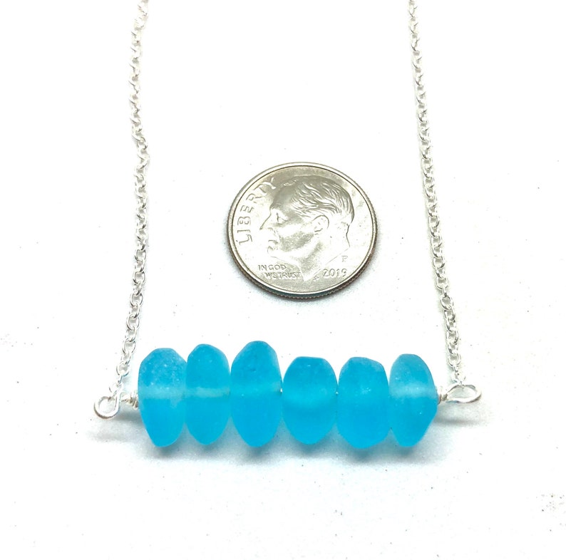 May include: A silver chain necklace with a row of light blue sea glass beads. The necklace is about the size of a dime.