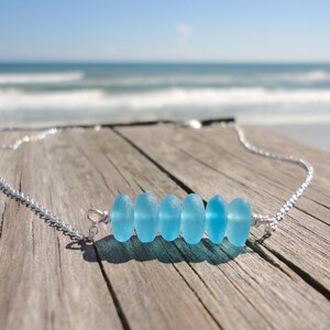 May include: A silver chain necklace with a row of six light blue sea glass beads.