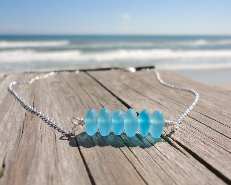 May include: A silver chain necklace with a row of six light blue sea glass beads.