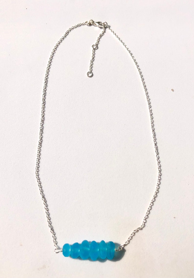 May include: A silver chain necklace with a row of light blue glass beads.
