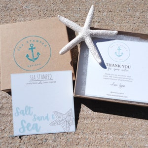 May include: A product presentation featuring a white starfish, a brown box with a teal anchor logo, and a white card with the text "Sea Stamped Designs". Another card reads "Salt, Sand & Sea". A thank you card is also visible.