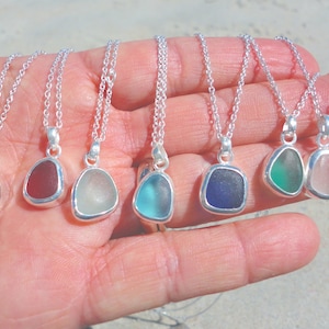 May include: Seven silver necklaces with different colored sea glass pendants. The pendants are all in the shape of a teardrop and are set in silver.