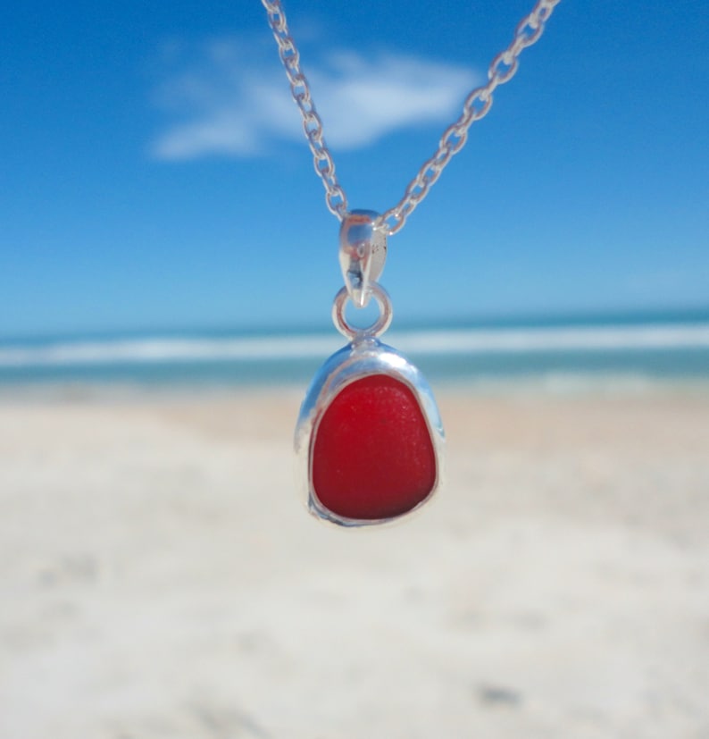 May include: A silver necklace with a red sea glass pendant. The pendant is shaped like a teardrop and has a smooth, polished surface.