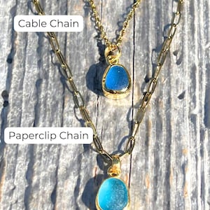 May include: Two gold necklaces with blue glass pendants. The top necklace has a cable chain and the bottom necklace has a paperclip chain.