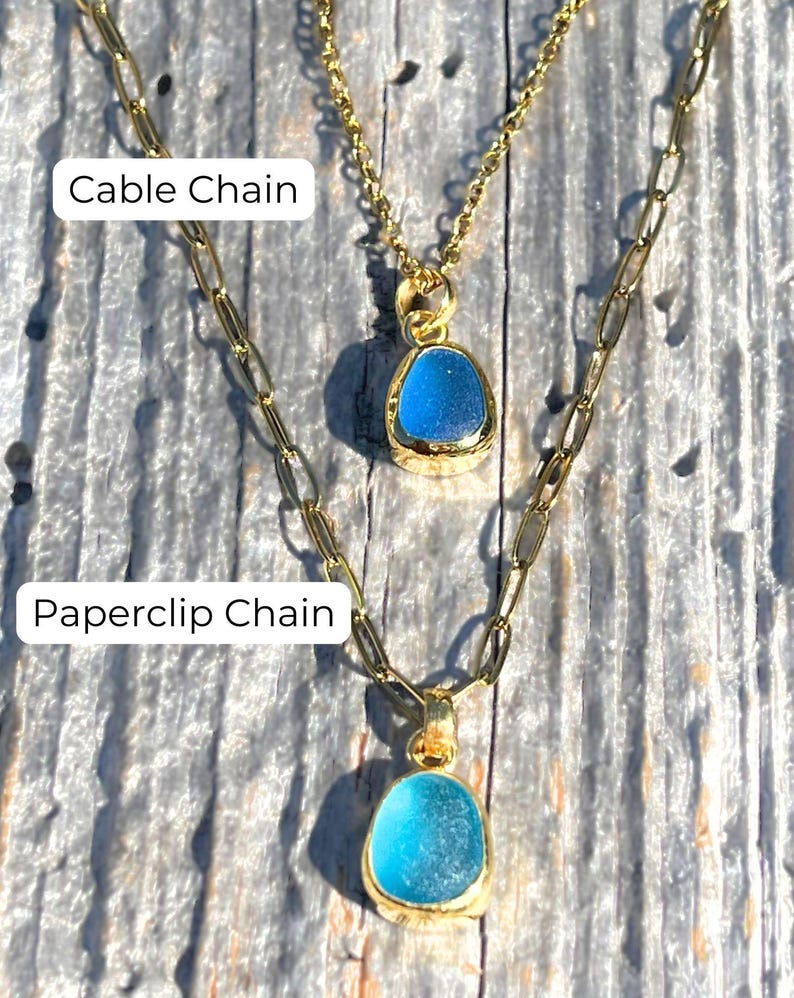 May include: Two gold necklaces with blue glass pendants. The top necklace has a cable chain and the bottom necklace has a paperclip chain.