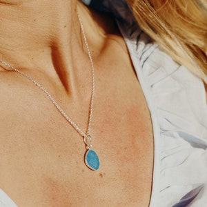 Op de afbeelding: Een zilveren ketting met een traanvormige hanger met een blauwe edelsteen.