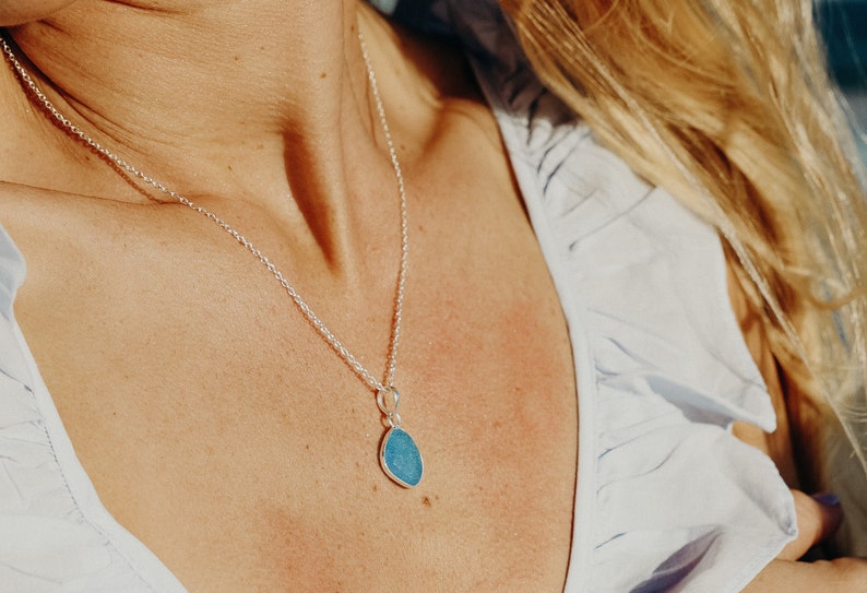 Op de afbeelding: Een zilveren ketting met een traanvormige hanger met een blauwe edelsteen.