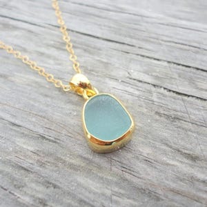 May include: A gold chain necklace with a light blue sea glass pendant. The pendant is set in a gold bezel.