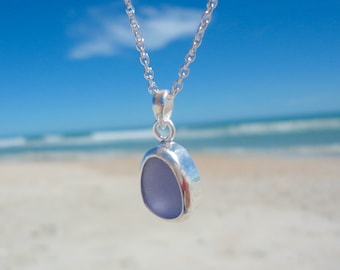 May include: A silver chain necklace with a pendant featuring a light blue piece of sea glass.