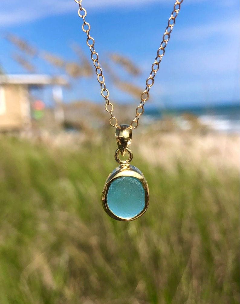 May include: A gold chain necklace with a light blue sea glass pendant
