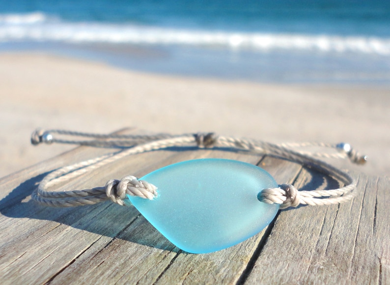 Peut inclure: Un bracelet en corde grise avec un pendentif en verre de mer bleu clair. Le bracelet est nou&eacute; et comporte des perles argent&eacute;es aux extr&eacute;mit&eacute;s.