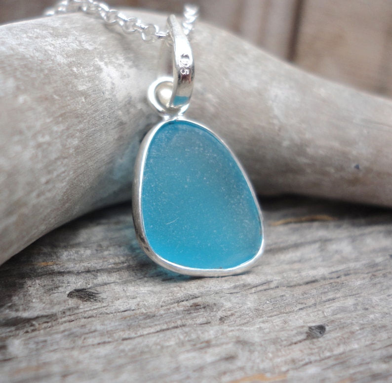 Op de afbeelding: Een zilveren ketting met een hanger met een lichtblauw stuk zeeglas.