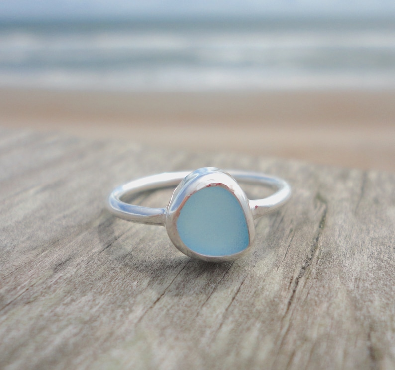 May include: A silver ring with a light blue sea glass stone set in the centre.