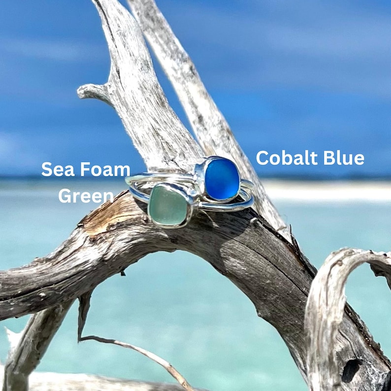 May include: Two silver rings with square sea glass stones. The ring on the left has a light green stone labelled "Sea Foam Green". The ring on the right has a cobalt blue stone labelled "Cobalt Blue".