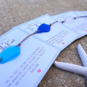 Puede incluir: Un conjunto de cuatro pulseras de recuerdo con abalorios de vidrio de mar y un mensaje de agradecimiento por ayudar a atar el nudo. El mensaje dice: "Gracias por ayudarnos a atar el nudo. Como el suave vaiv&eacute;n de las olas del oc&eacute;ano, tu apoyo inquebrantable ha significado el mundo para nosotros. Te estoy profundamente agradecido por tenerte como mi dama de honor."