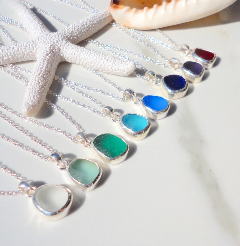 May include: A set of nine silver necklaces with teardrop-shaped sea glass pendants in various shades of blue, green, and purple.
