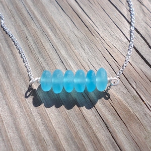 May include: A silver chain necklace with a row of six light blue sea glass beads.