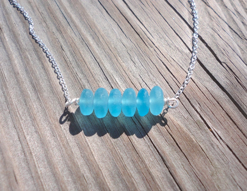 May include: A silver chain necklace with a row of six light blue sea glass beads.