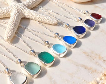 May include: A collection of eight silver necklaces, each featuring a single smooth, rounded sea glass pendant in a different color, including white, light green, dark green, light blue, bright blue, dark blue, purple, and deep red.