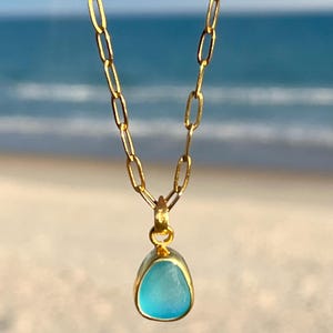 May include: A gold chain necklace with a pendant featuring a light blue sea glass stone.