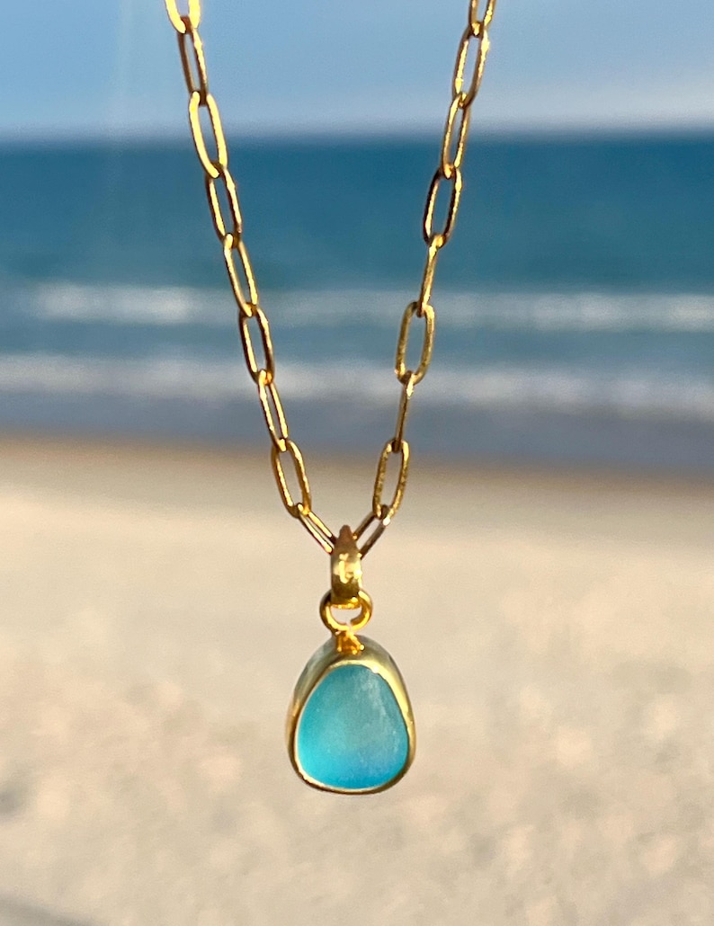 May include: A gold chain necklace with a pendant featuring a light blue sea glass stone.