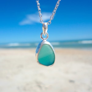 May include: A silver chain necklace with a pendant featuring a light blue and green sea glass piece.