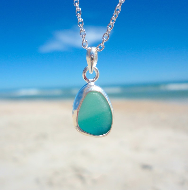 May include: A silver chain necklace with a pendant featuring a light blue and green sea glass piece.