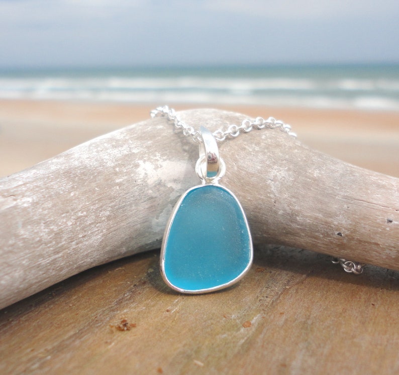Op de afbeelding: Een ketting met een turquoise zeeglas hanger aan een zilveren ketting. De hanger heeft de vorm van een traan en is gezet in een zilveren bezel.