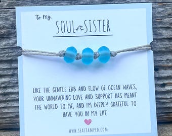 Könnte beinhalten: Eine Karte mit dem Text "To my Soul Sister" und einer Botschaft über die Bedeutung von Freundschaft. Die Karte ist mit einem hellblauen Perlenarmband verziert.
