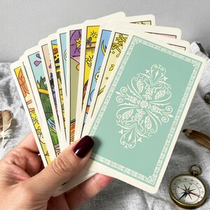 Rider Waite tarot cards back design with classic green patterned backs, tarot deck held in hand with spiritual accessories