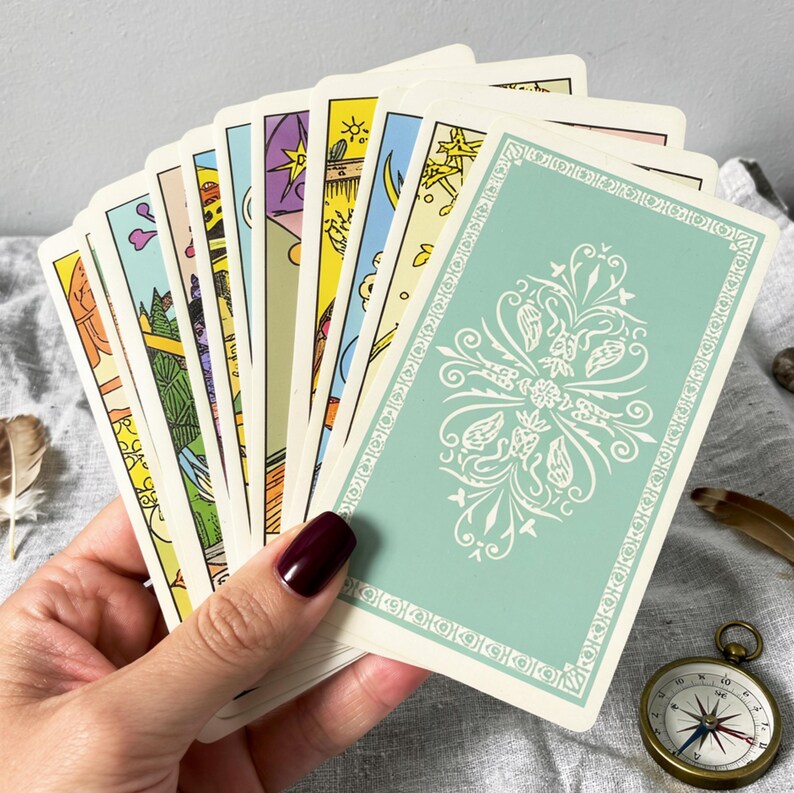 Rider Waite tarot cards back design with classic green patterned backs, tarot deck held in hand with spiritual accessories