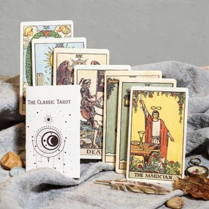 Rider Waite tarot cards arranged upright including The Magician card, Classic Tarot guidebook and spiritual tarot reading setup