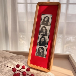 Könnte beinhalten: Ein Holzrahmen-Fotodisplay mit rotem Hintergrund. Das Display enthält vier Schwarz-Weiß-Fotos im Fotokabinenstil einer Person. Der Rahmen hat eine hellbraune Holzoberfläche.