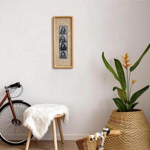 May include: A rectangular wooden picture frame holding four black and white portrait photographs. The frame is mounted on a white wall. A bicycle, a stool with a white fur cover, and a potted plant are in the foreground.