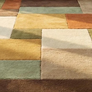 Hand-tufted patchwork area rug placed in a well-lit living room with mid-century modern furniture. The rug’s thick wool pile and earthy color blocks create a warm and inviting ambiance. Natural sunlight highlights the texture and craftsmanship, making it a perfect centerpiece for modern interior design.
