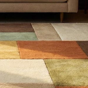 Luxury handmade wool rug with a modern patchwork layout, designed for living rooms and bedrooms. The geometric pattern and warm tones complement wooden interiors and neutral furniture, adding depth, warmth, and elegance to the space.
